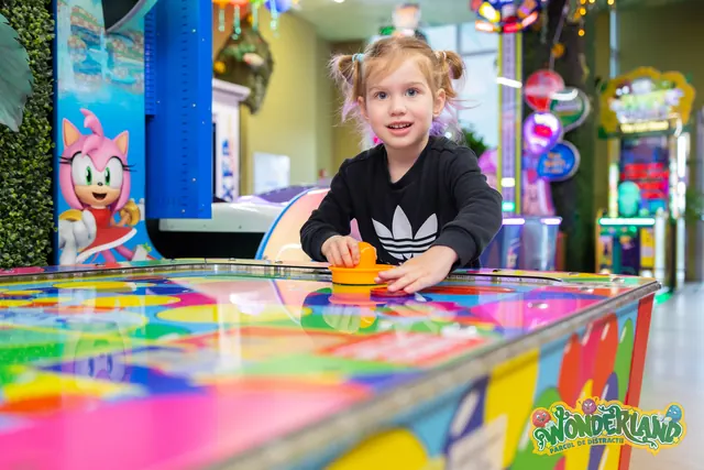 Un copil ține un mâner portocaliu la o masă de air hockey viu colorată.